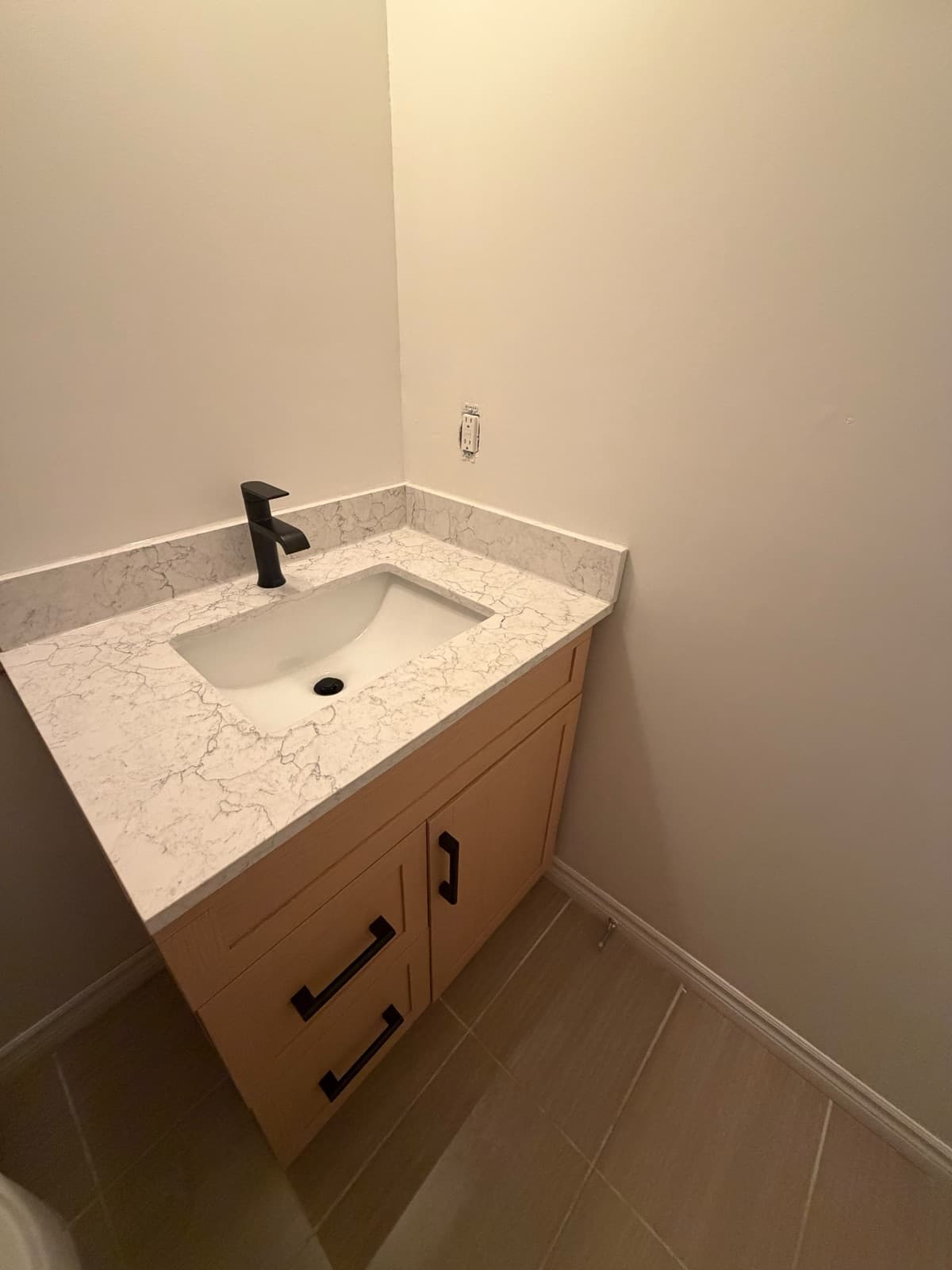 Wood vanity with quartz top and matte black faucet in a powder room